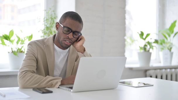 Fáradt afrikai férfi szundikál, miközben ül az irodában Laptop - Fotó, kép