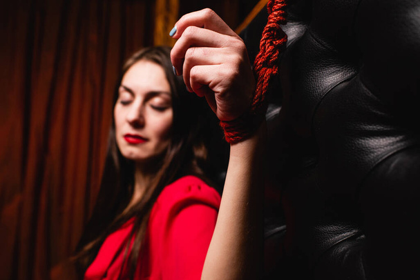 Žena připoutaná k posteli červenými provazy. Detailní záběr ženské ruky přivázané k posteli. - Fotografie, Obrázek