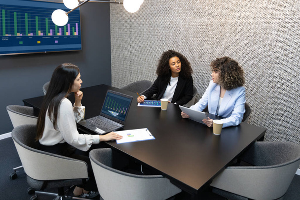 Multiculturele zakenvrouwen die tijdens een vergadering formele kleren dragen die in een groot bureau zitten. - Foto, afbeelding