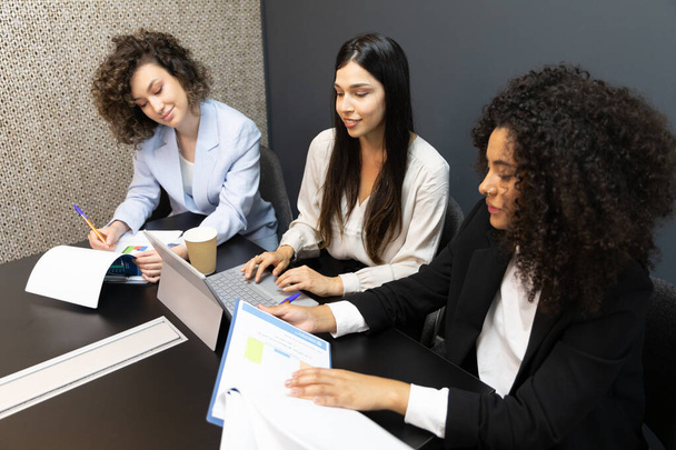 Jóvenes mujeres de negocios que usan tabletas digitales y hacen papeleo durante una reunión. - Foto, Imagen