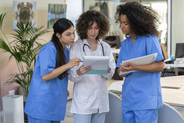 Nuori nainen lääketieteellisen työn joukkue yllään sininen univormu hymyillen ja katsoen toisiaan. - Valokuva, kuva