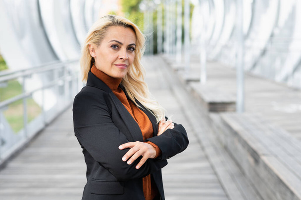 Adult blonde business woman standing with her arms crossed looking at camera in a urban landscape - Φωτογραφία, εικόνα