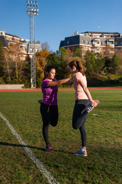 two young women doing stretching on the grass of a running track before playing sports - Foto, immagini
