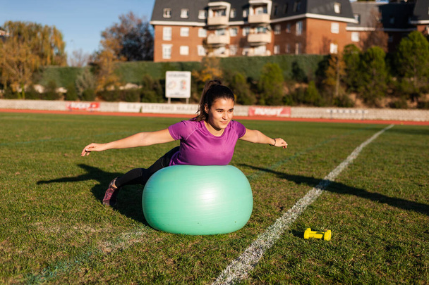 young woman doing exercise with a fitball on the grass - 写真・画像