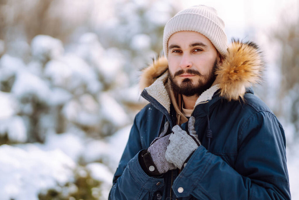Handsome bearded young  man standing outdoors fur hood in winter season forest. Season holiday leisure. Nature. - 写真・画像