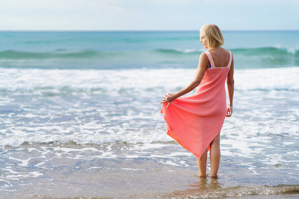 volwassen vrouw genieten van haar vrije tijd kijken naar de zee van de oever van het strand. - Foto, afbeelding