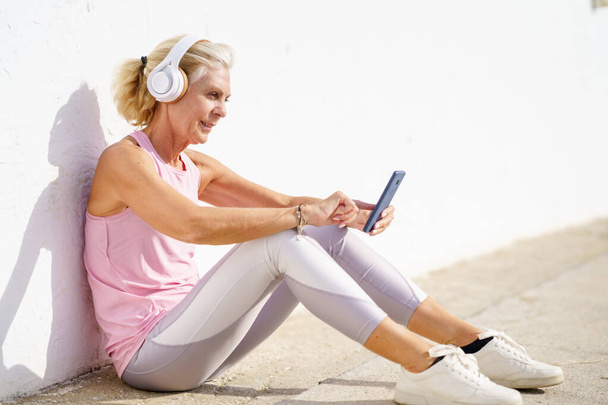 Зрелая спортивная женщина взяла перерыв, чтобы проверить фитнес-приложение на своем смартфоне - Фото, изображение
