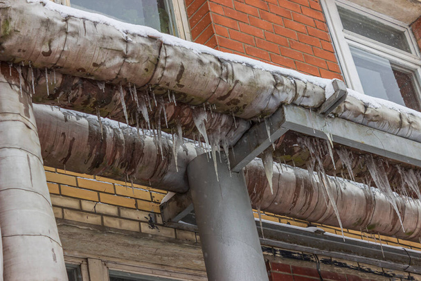 street lighting. a building through which a metal pipe wrapped with a thermal coating passes. there are damages and deformations, water flows and freezes and icicles have formed. - Foto, immagini