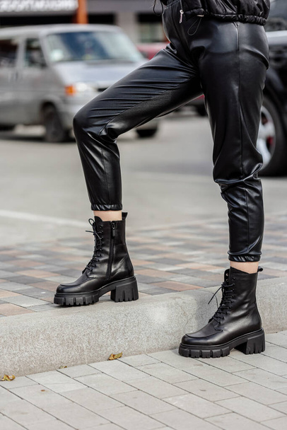 Una mujer delgada en botas de cuero negro, pantalones negros. Colección de zapatos para mujer - Foto, imagen