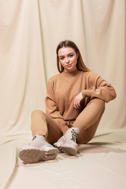 Jonge model vrouw in gebreide pak, beige leren laarzen en trui poseren binnen - Foto, afbeelding