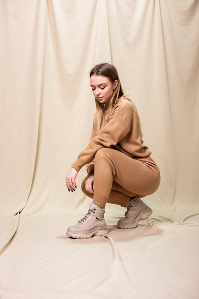 Jovem mulher modelo em terno de malha, botas de couro bege e suéter posando dentro de casa - Foto, Imagem