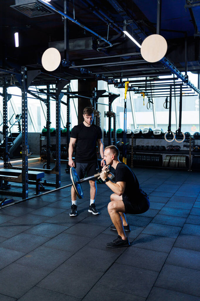 Homme sportif faisant des exercices avec l'aide de son entraîneur personnel dans une salle de gym publique. - Photo, image