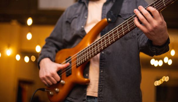 Ένας νεαρός με μούσι παίζει μπάσο κιθάρα με πέντε χορδές. - Φωτογραφία, εικόνα