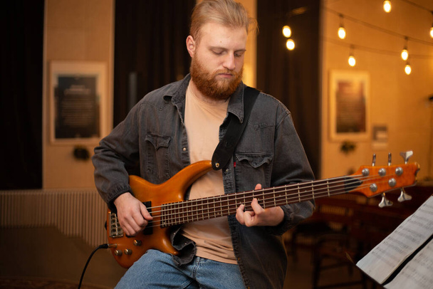 Молодий хлопець з бородою грає на бас-гітарі з п'ятьма струнами
 - Фото, зображення