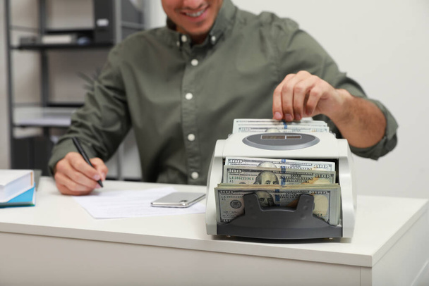 Man using banknote counter at white table indoors, closeup - Foto, afbeelding