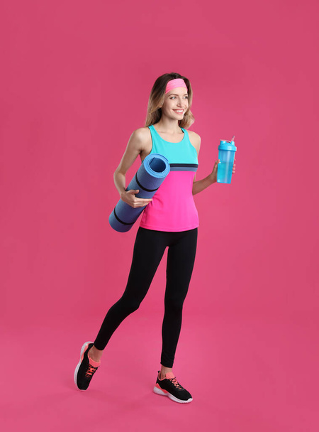 Beautiful woman with yoga mat and shaker on pink background - Foto, afbeelding