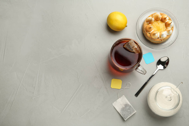Composição de leigos planos com saco de chá em xícara de cerâmica de água quente e sobremesa em mesa cinza. Espaço para texto - Foto, Imagem