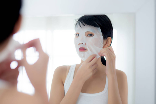 Gyönyörű fiatal ázsiai nő lapos arc maszk és látszó tükör otthon, szépség lány alkalmazása kozmetikai és smink bőrápoló arc ránc, kezelés és hidratáló, egészség és wellness. - Fotó, kép