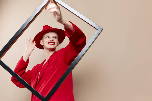 μοντέρνα γυναίκα με ξύλινο πλαίσιο που θέτει κόκκινο κοστούμι μπεζ φόντο - Φωτογραφία, εικόνα