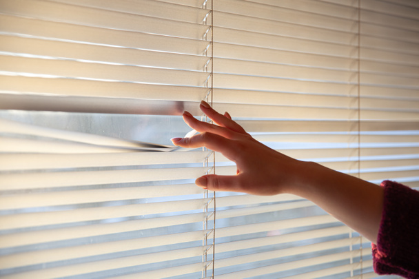 Vrouwen hand nemen een kijkje door het raam blinds. - Foto, afbeelding