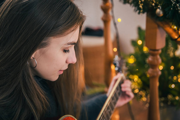 Młoda kobieta grająca na gitarze siedząca na schodach w domu. - Zdjęcie, obraz