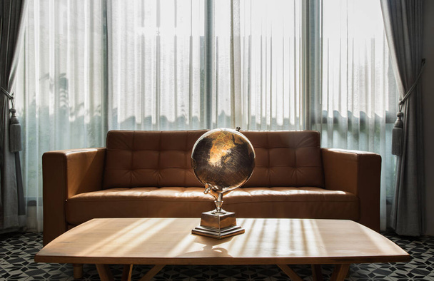 Chiang Rai,Thailand - Sep 06, 2020 : Replica globe on wooden coffee table front to brown leather sofa on background of white curtains in living room with copy space. No focus, specifically. - Foto, Imagen