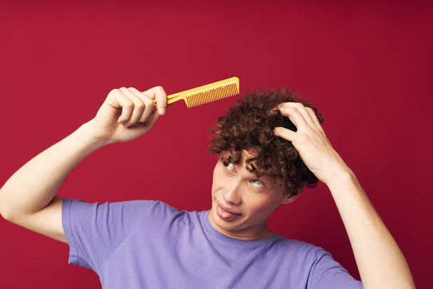 portrait of a young curly man in purple t-shirts with a comb isolated background - Фото, зображення