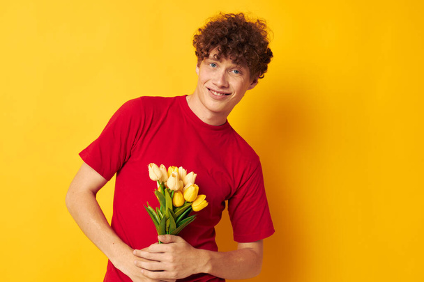 Young curly-haired man in a red T-shirt with a bouquet of flowers Lifestyle unaltered - Zdjęcie, obraz