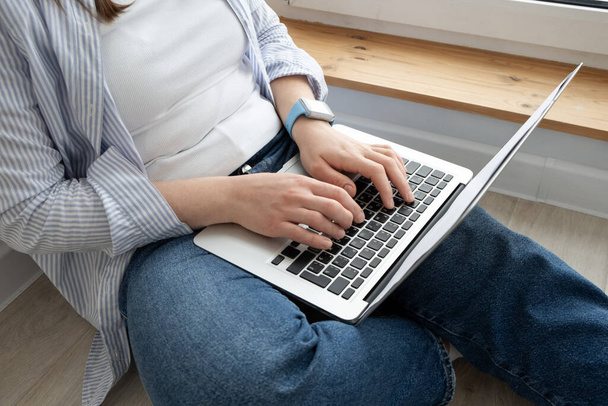 Middle-aged woman working from home. Girl using laptop at home, sitting near a large window. Remote work concept - Photo, Image
