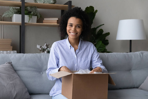 Smiling young african american woman unpacking carton box. - 写真・画像
