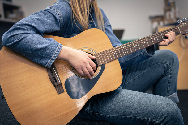 Primer plano, una mujer en traje de mezclilla toca la guitarra. - Foto, Imagen