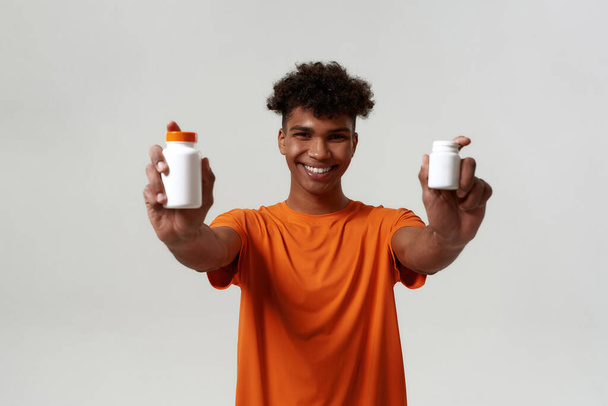 Black smiling man showing jars with medical pills - Foto, afbeelding