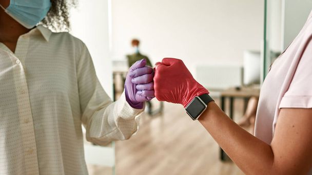 Women bumping fists in medical gloves in office - Fotografie, Obrázek