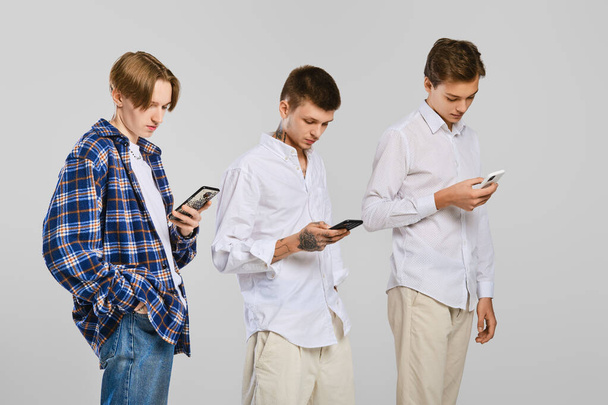 Three young men stand in profile and watch on their mobile - Foto, Imagen