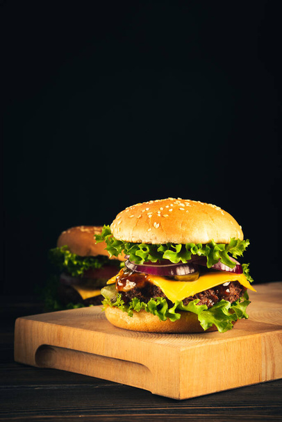 Tasty hamburgers on wooden board on dark background. - Valokuva, kuva