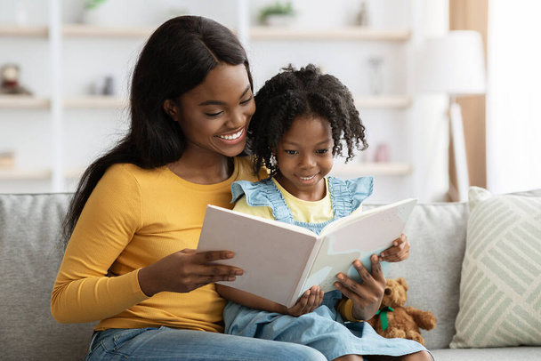 Loving black mom reading book to her cute little daughter at home - Fotoğraf, Görsel