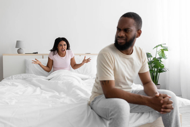 triste joven negro hombre escuchar esposa, mujer asustándose y grita a infeliz marido, juro en dormitorio interior - Foto, Imagen