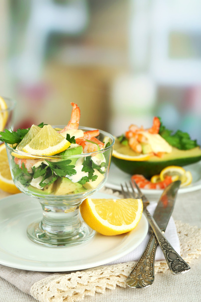 Tasty salads with shrimps and avocado in glass bowl and on plate, on table, on bright background - Foto, imagen