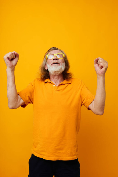 Senior grey-haired man yellow t-shirt and glasses posing yellow background - Фото, изображение