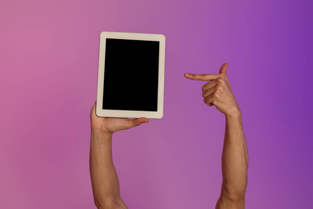 Cropped view of millennial man pointing at tablet computer with empty black screen in neon light, mockup - Фото, изображение