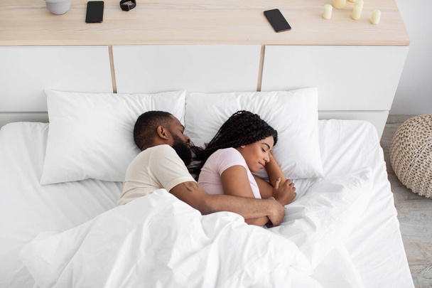 Millennial black lady and man lie on white soft bed, hugging, sleeping and relax at night in bedroom interior - Foto, immagini