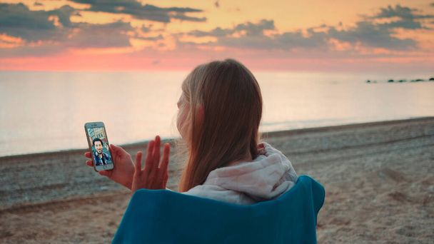 Молода жінка робить відеодзвінок зі смартфоном на березі моря
 - Фото, зображення