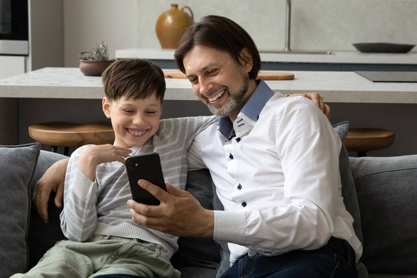 Happy dad and cheerful teen kid using, sharing smartphone together - Foto, Imagem
