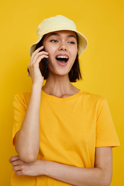 young woman yellow t-shirt and Hat summer style with phone yellow background - Fotoğraf, Görsel