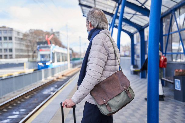 Male pensioner looking at the train and carrying his luggage while standing - Foto, afbeelding