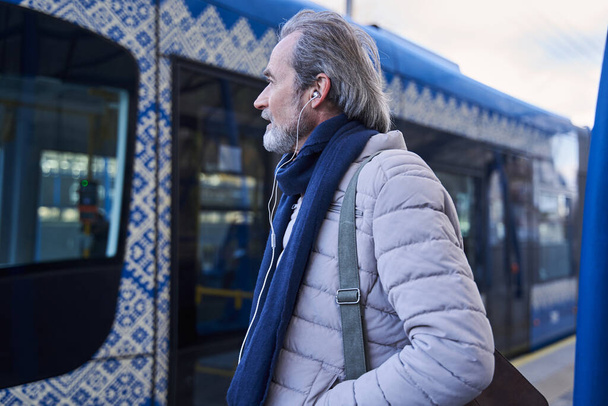 Man wearing earphones walking through the railway station and listening his favorite songs - Фото, изображение