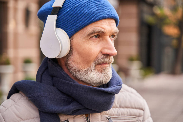 Calm senior bearded man looking away while listening music - Foto, Bild