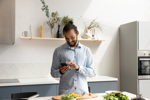 Щасливий чорний шеф-кухар використовує мобільний телефон на домашній кухні
 - Фото, зображення