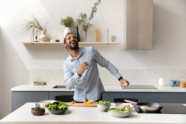 Happy cheerful millennial chef guy cooking, dancing to music - Photo, image