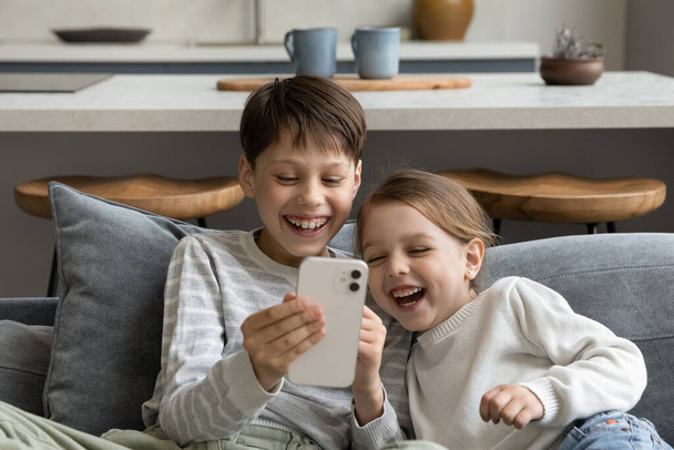 Happy cheerful sibling kids watching funny media on smartphone - Photo, Image
